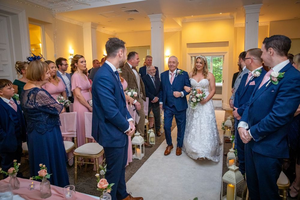 Bride walking down the aisle with her father during an elegant indoor wedding ceremony.