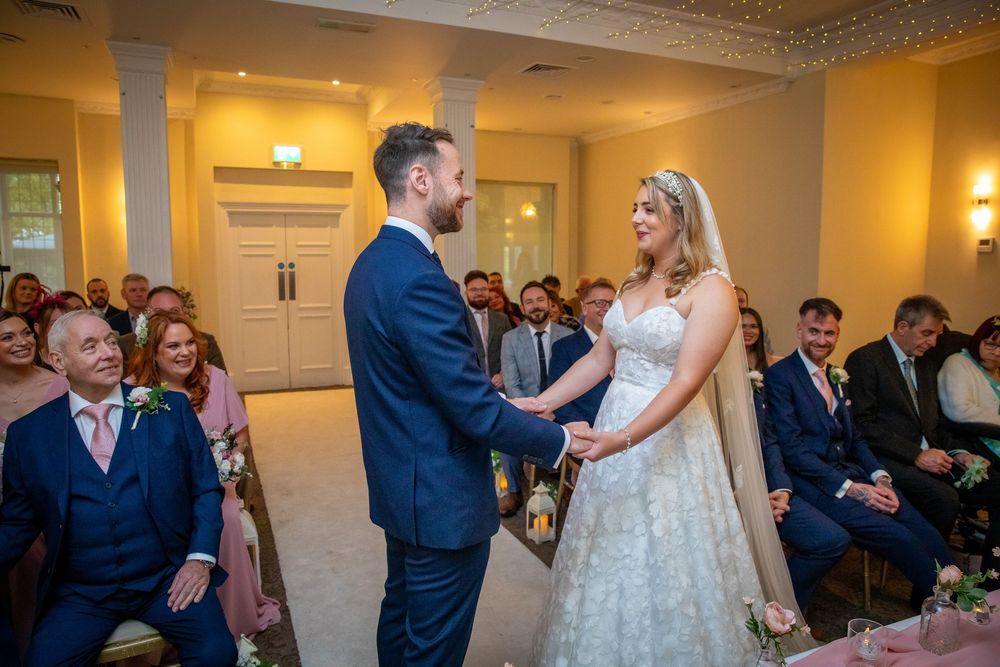 Bride and groom holding hands and exchanging vows during their wedding ceremony indoors.