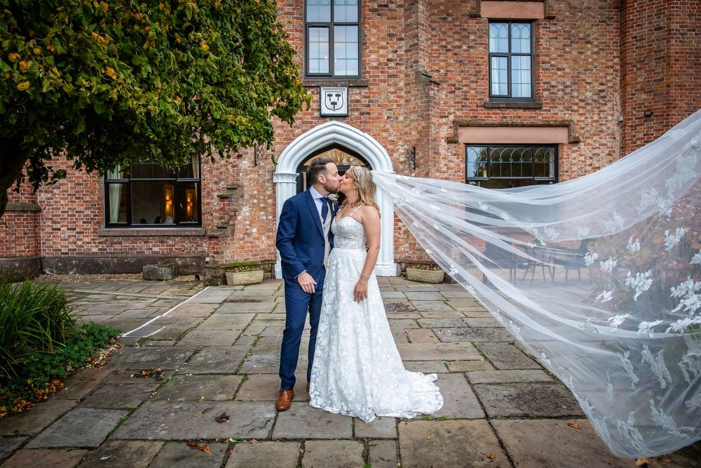 Bride and groom kissing with the bride's veil flowing in the wind outside a brick venue.