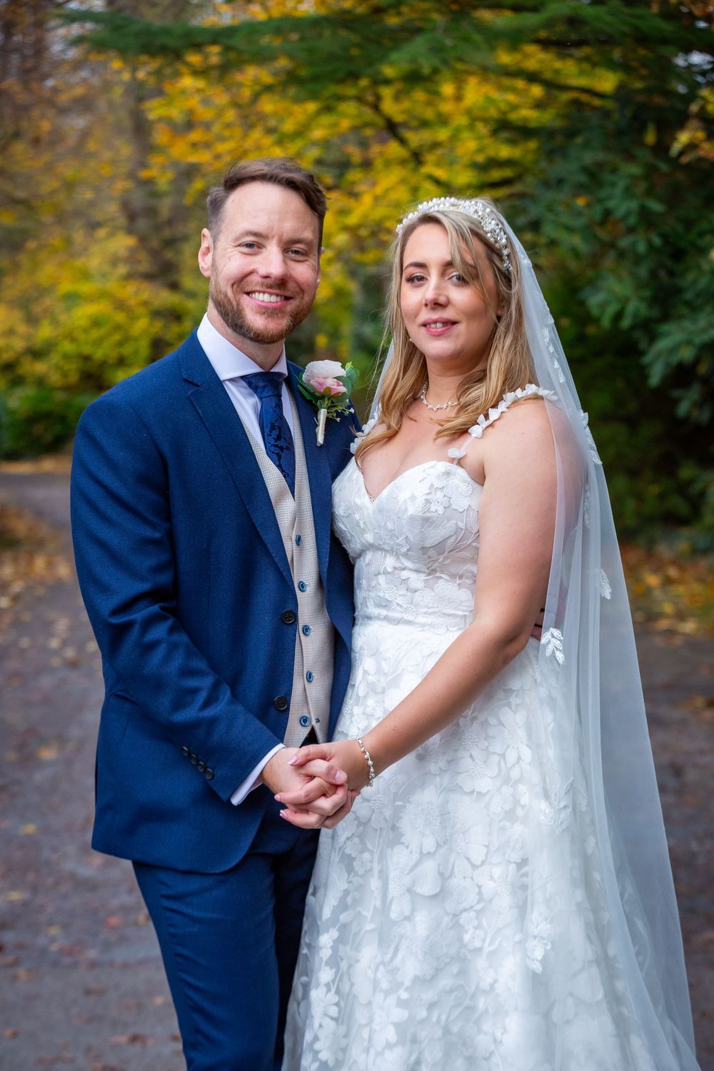 Smiling bride and groom holding hands in an autumn woodland setting on their wedding day.