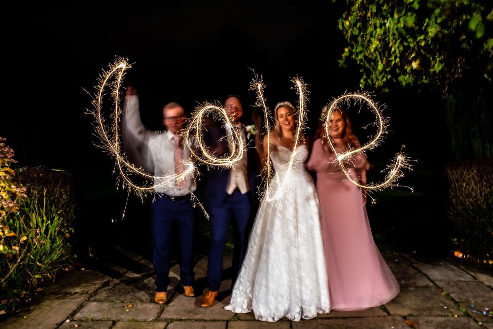 Bride, groom, and guest spelling LOVE with sparklers at night during wedding celebrations.