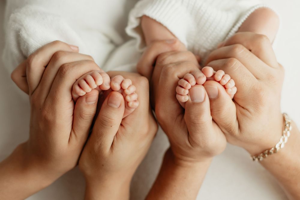 Twin newborn girls, closeup of their feet in parents' hands, taken by Jen Knightstep, Photographer