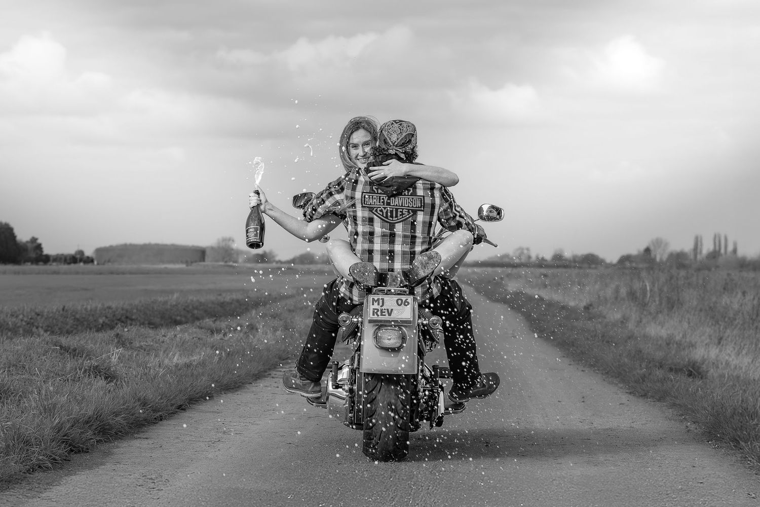 A motorcycle rider cruises down a scenic rural road with fields stretching into the distance on a cloudy day.