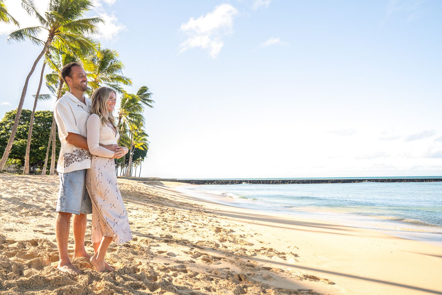 A couple stands together on a tropical beach with palm trees and ocean views on a sunny afternoon.
