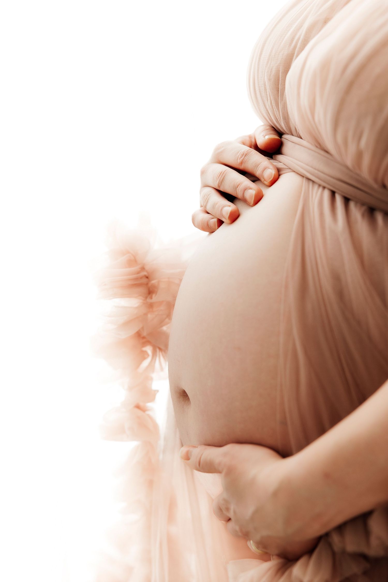 A gentle sepia-toned maternity photo showing hands cradling a pregnant belly draped in soft fabric.