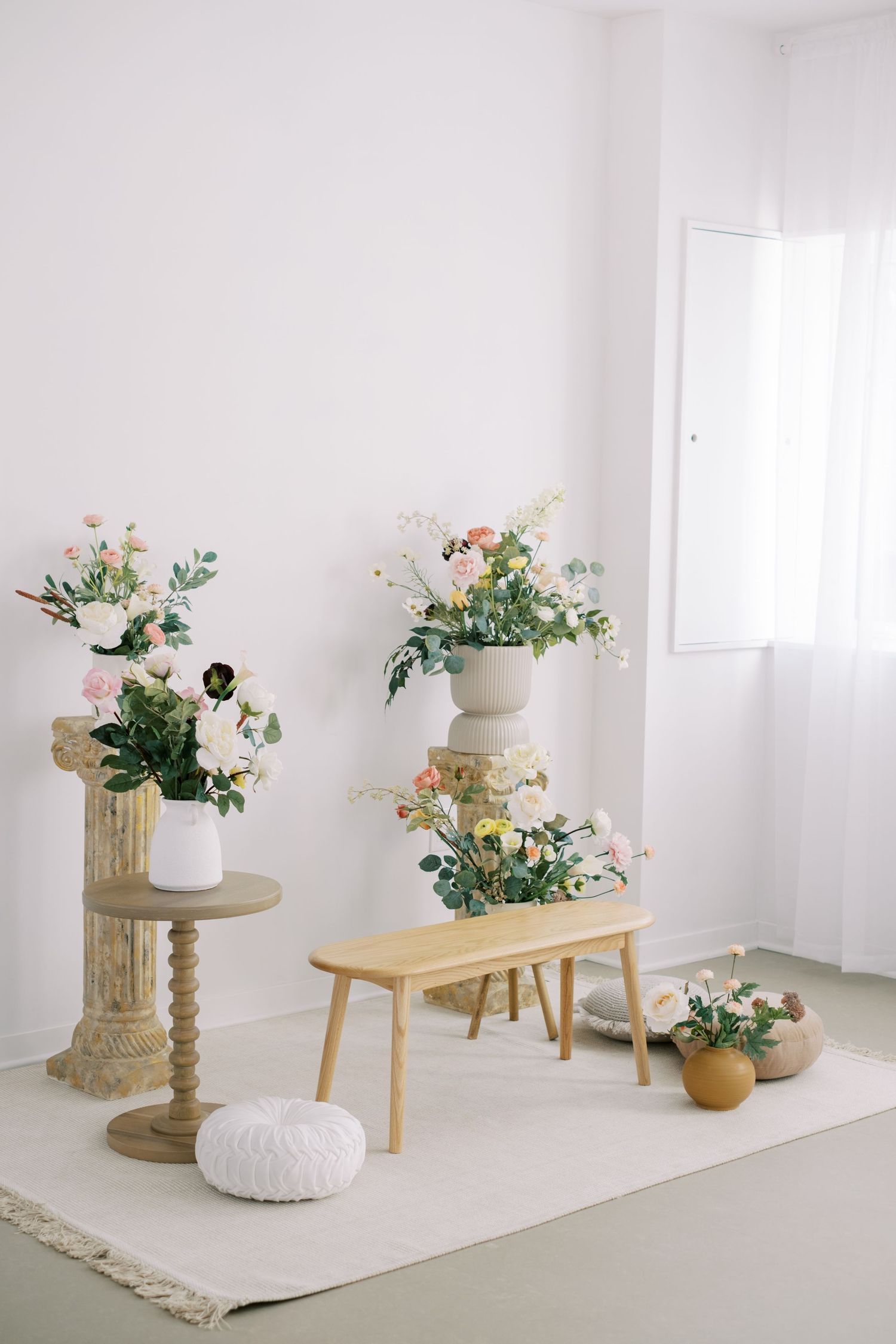 Minimalist white room interior with floral arrangements on wooden furniture and a beige area rug.