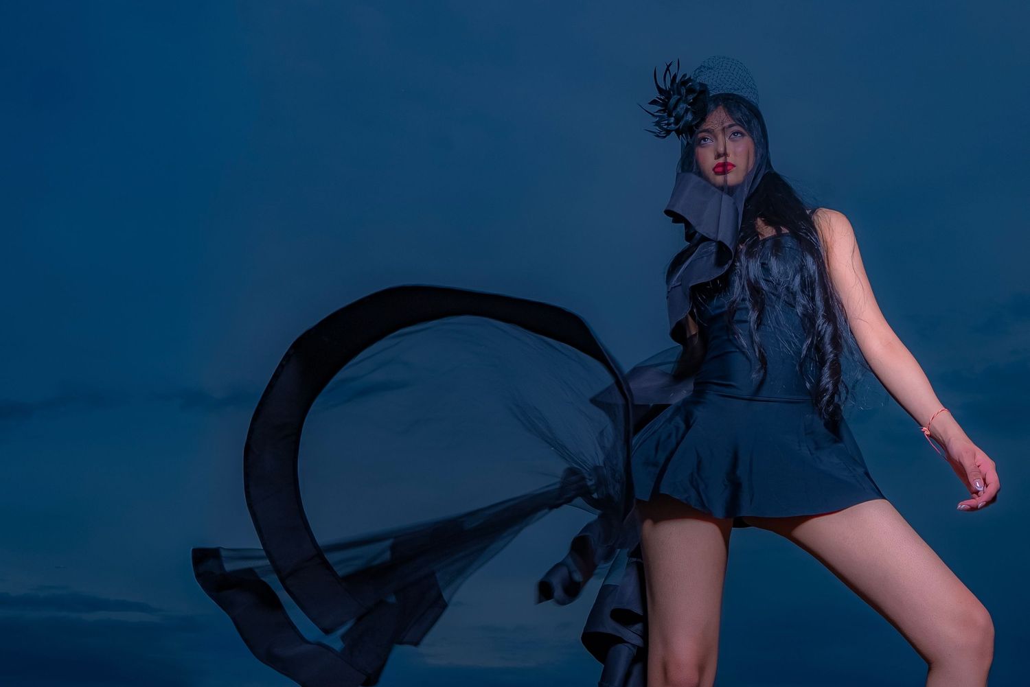 Artistic fashion photo of model in blue dress against dark background with dramatic lighting.