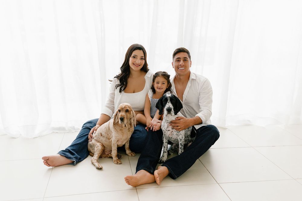 Family wearing white clothing poses together against a white background for professional studio portraits.