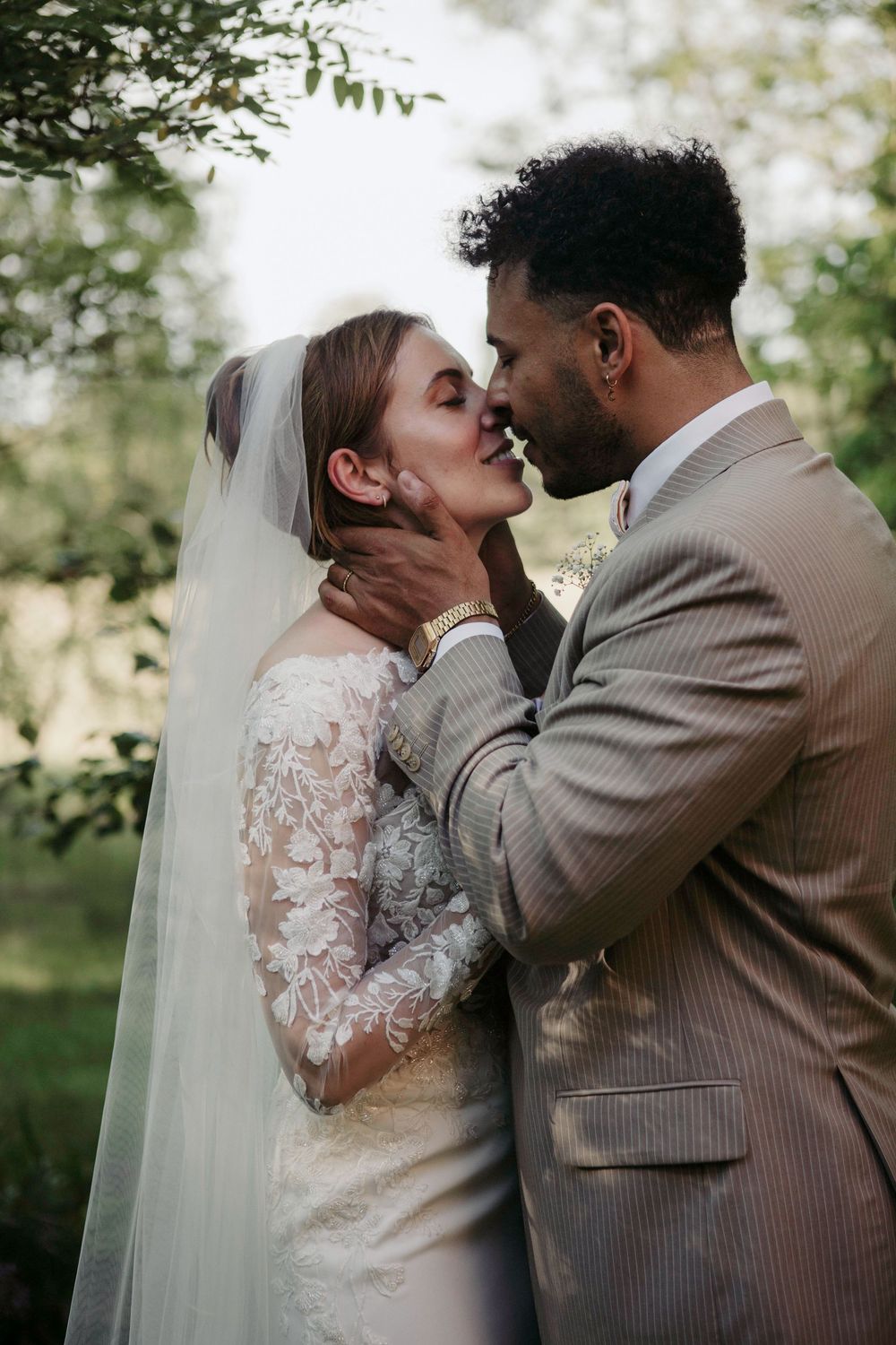 A bride and groom share a romantic almost-kiss outdoors, with the groom tenderly holding her face on their wedding day.
