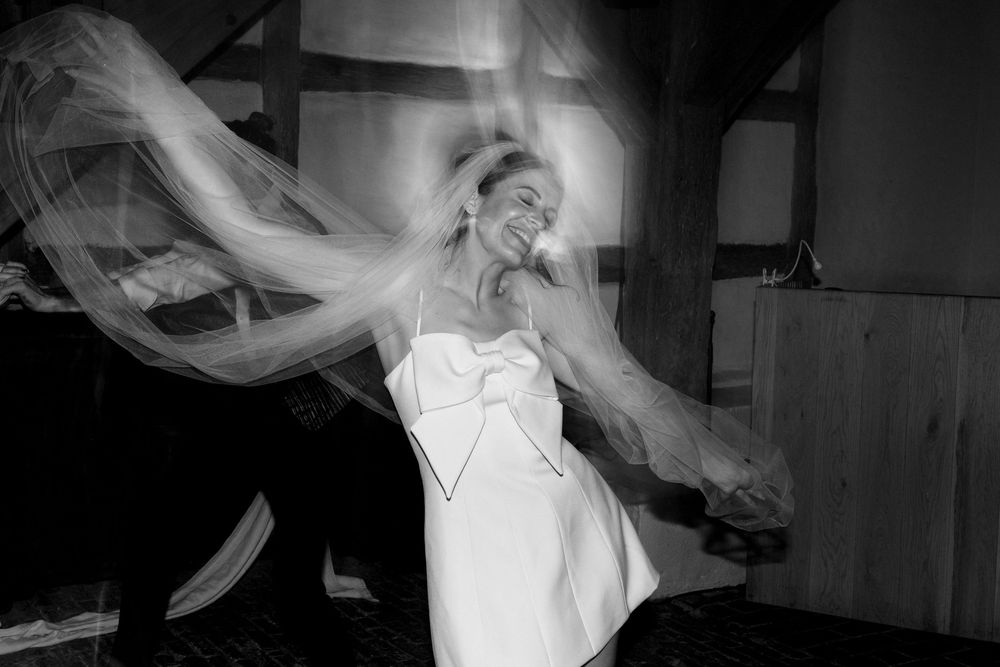 Black and white photo of a bride in a white dress twirling with her veil flowing around her.