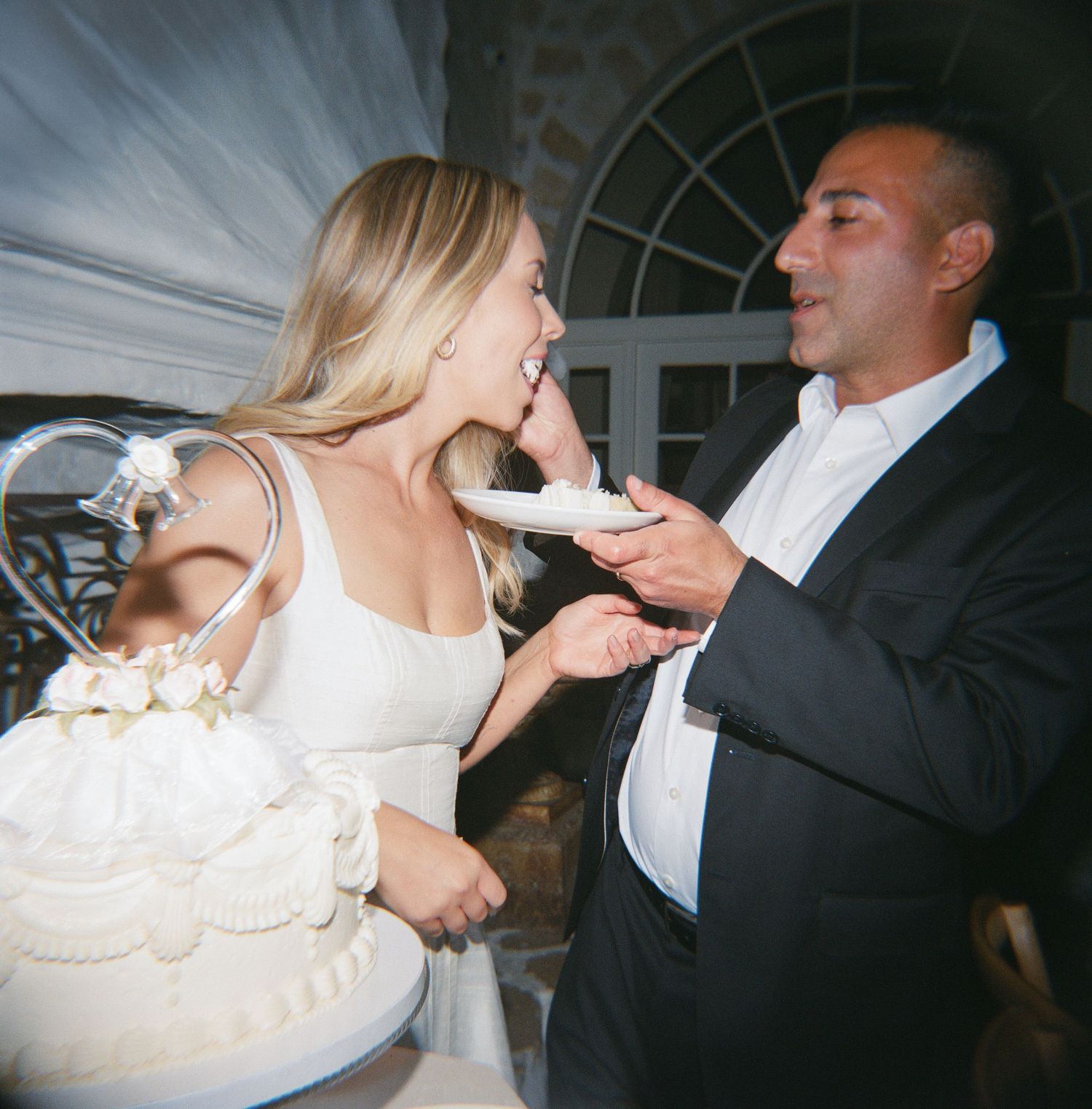 Bride and groom sharing wedding cake at reception, smiling joyfully.