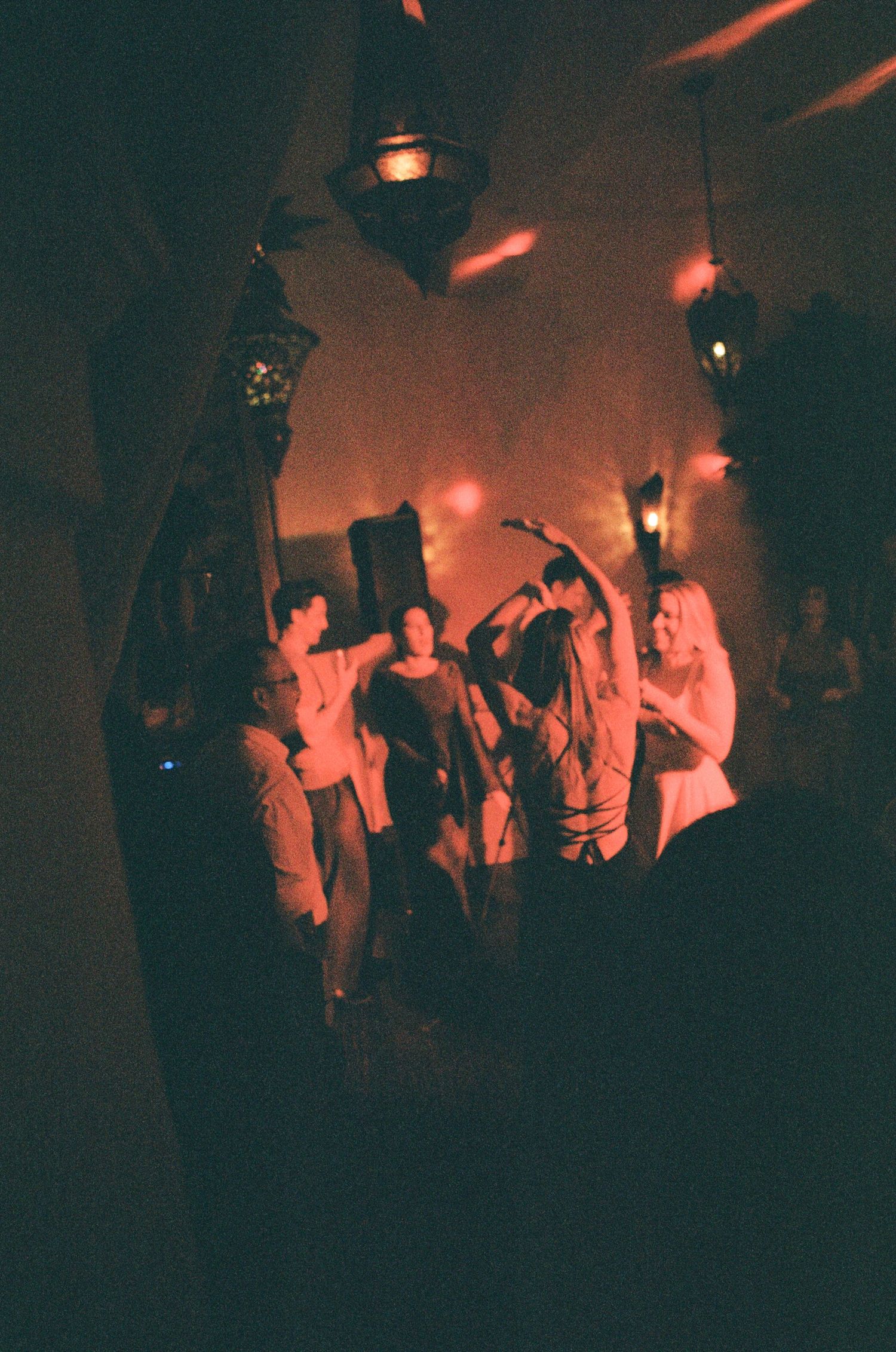 Guests dancing under warm Moroccan lanterns at a dimly lit wedding reception party.