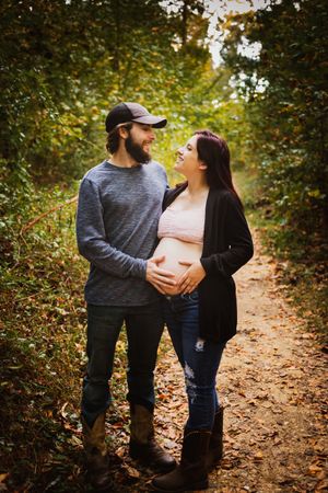 Couple sharing a tender moment on a leaf-covered forest path, woman visibly pregnant, during autumn.