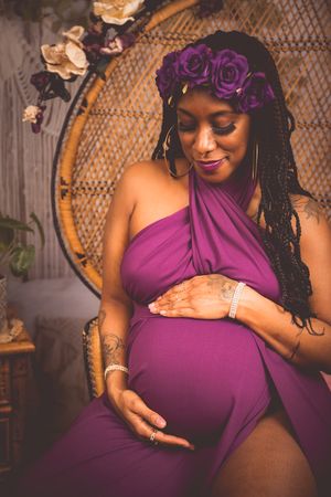 Pregnant woman in purple dress and floral crown cradles baby bump in boho maternity photo session.