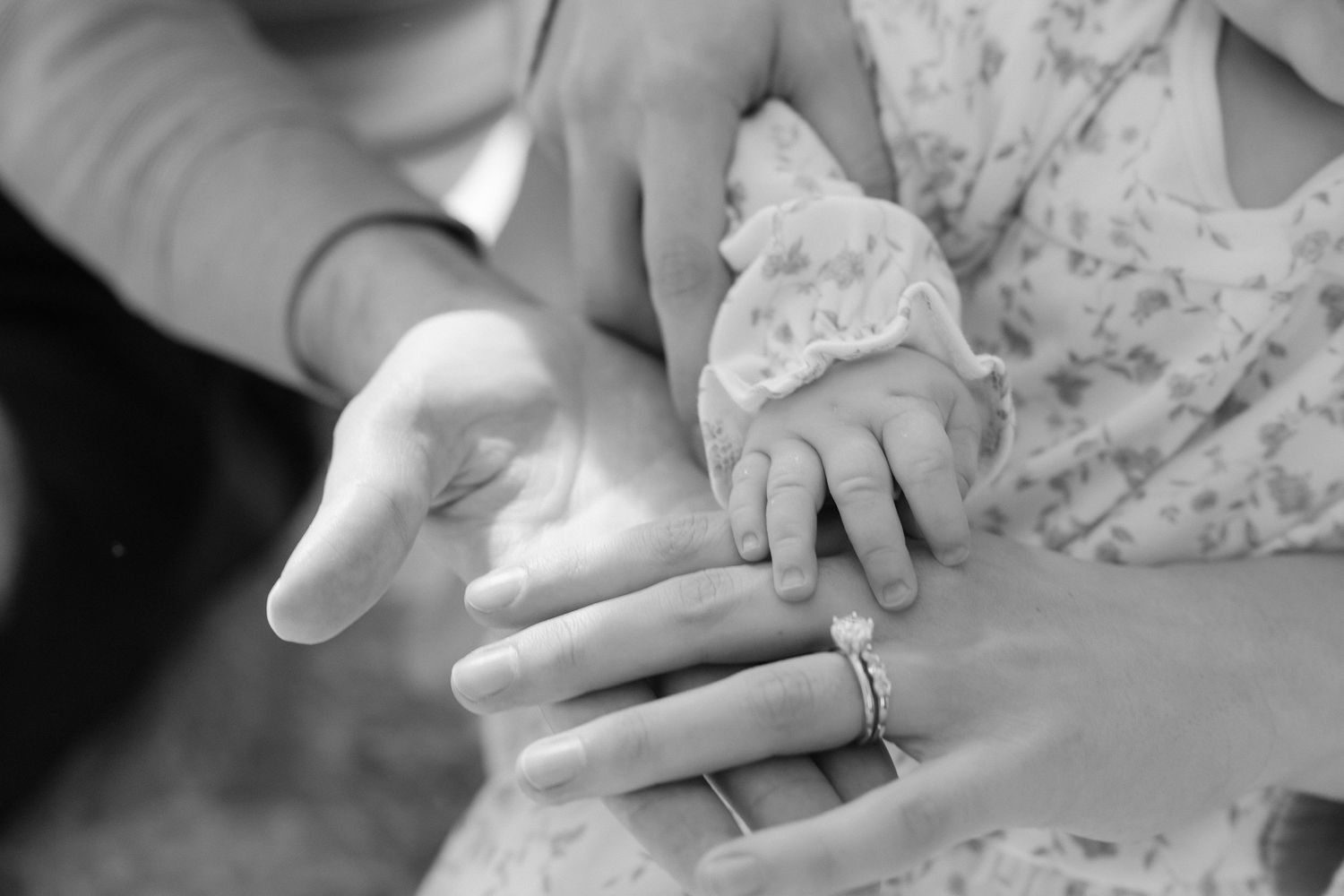 Black and white photo of a newborn baby's tiny hand resting on parents' hands, showing wedding rings.