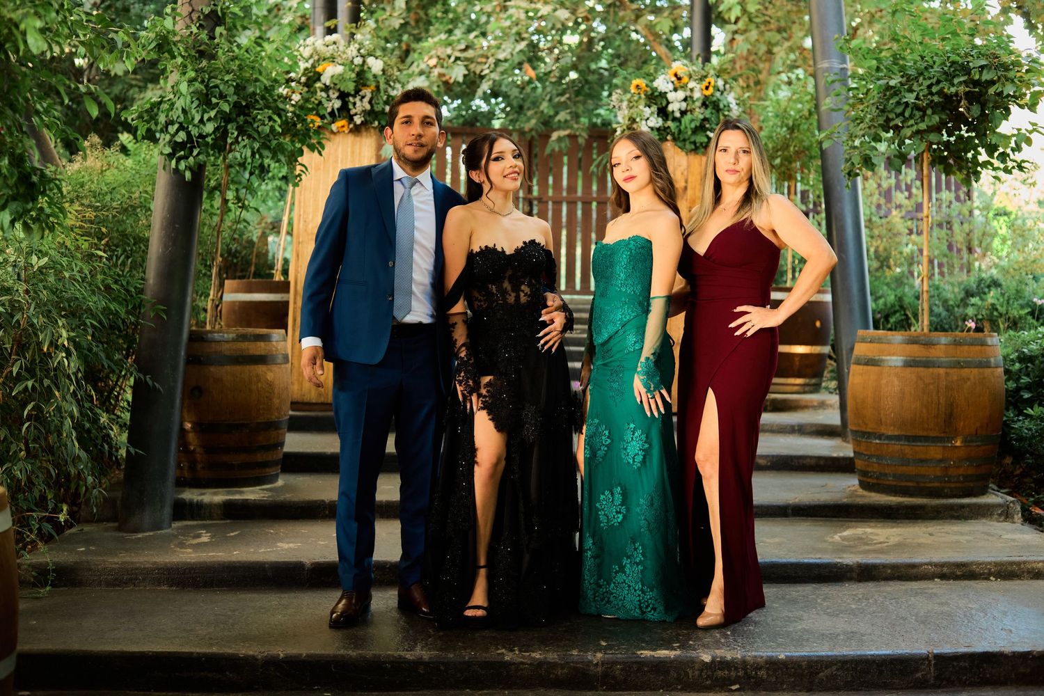 Wedding party members in formal attire pose together in an outdoor garden venue setting.