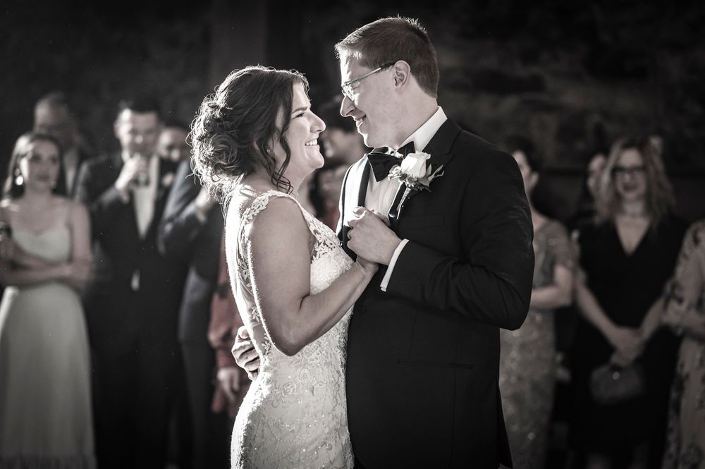 A couple shares a romantic first dance at their wedding reception surrounded by guests with cameras.