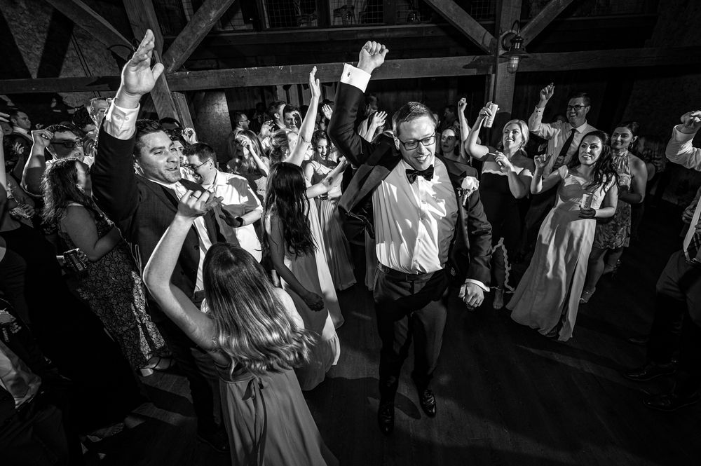 A large crowd of wedding guests dancing together on a dance floor during an evening reception celebration.