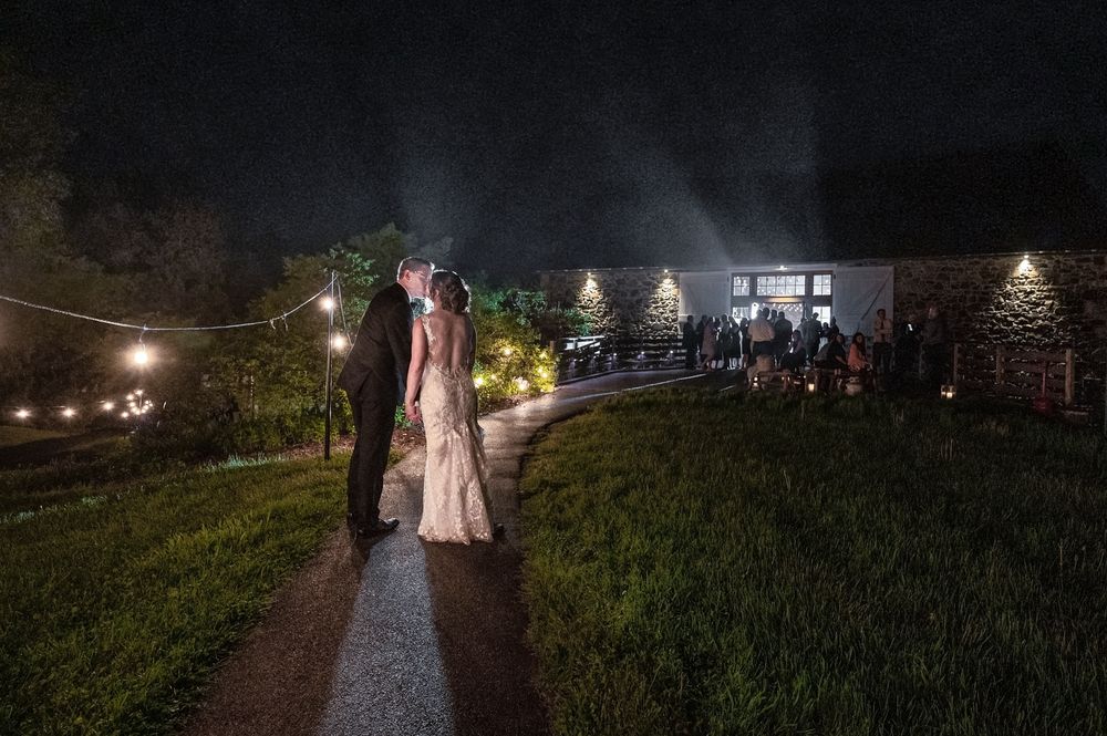 String lights illuminate a romantic outdoor evening wedding ceremony on a grassy hillside.