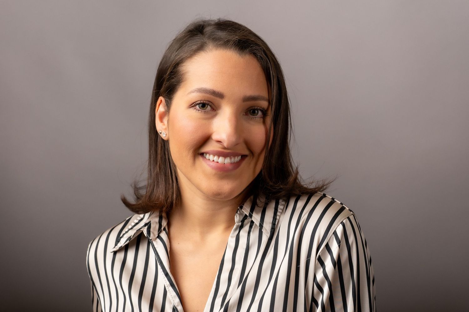 A person wearing a black and white striped shirt smiles while posing against a gray background.