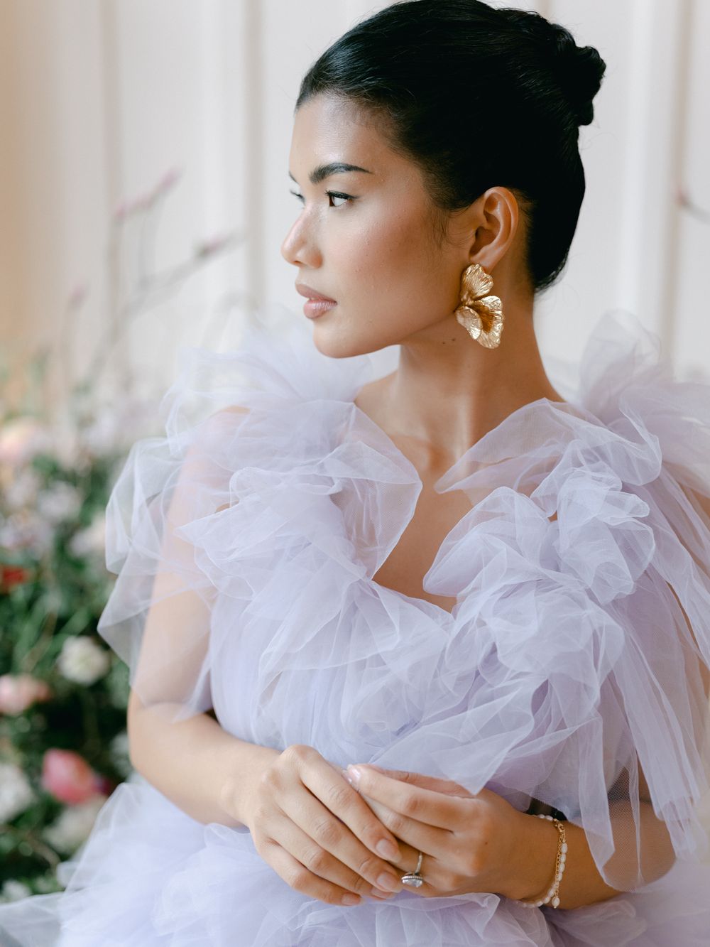 A bride in a white tulle gown with ruffled shoulders poses elegantly against a light background in a series of portraits.