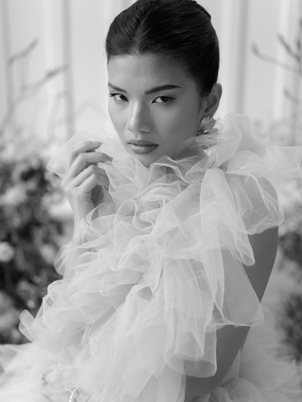 Black and white portrait showcasing dramatic ruffled tulle neckline against soft floral background.