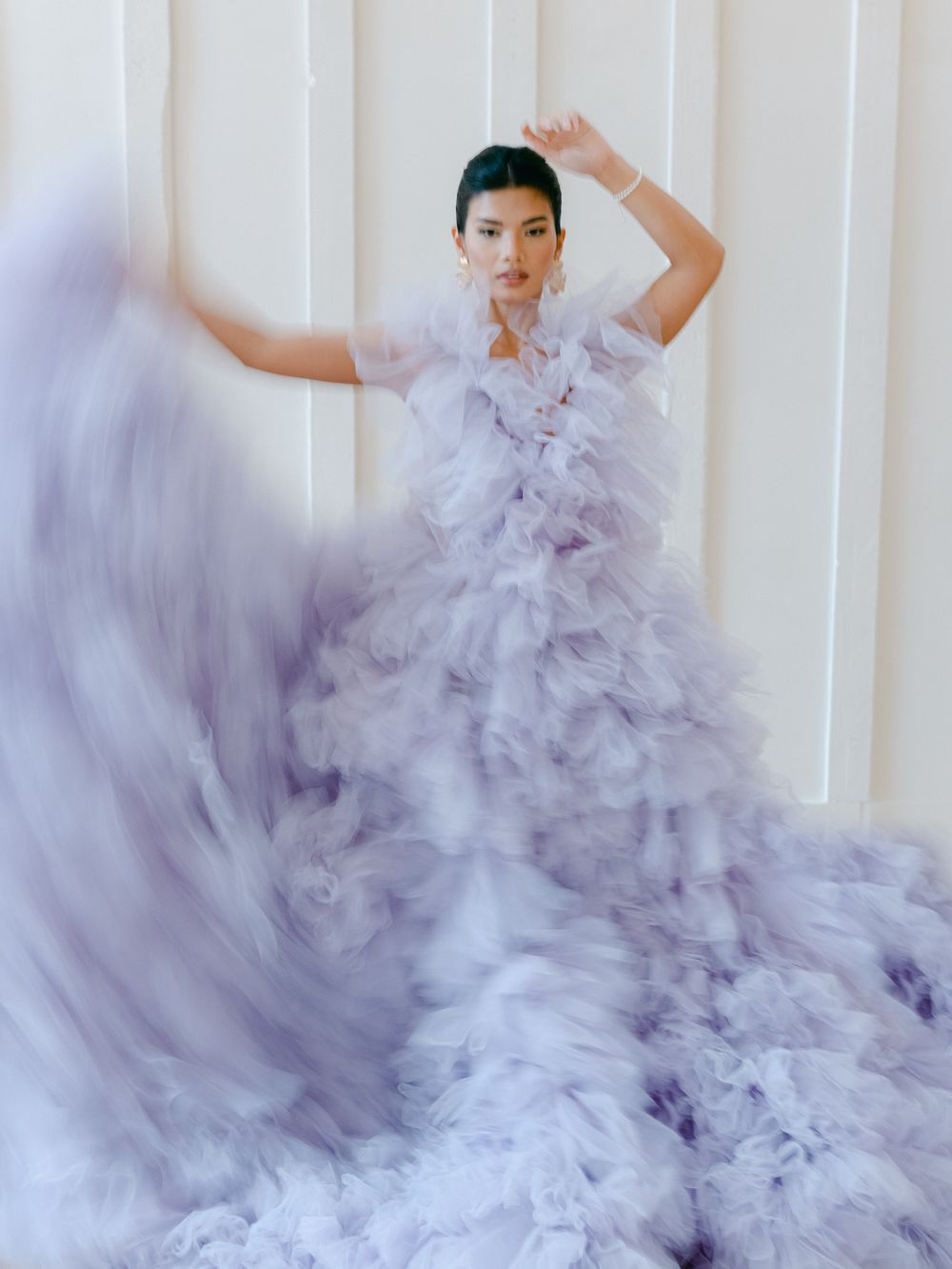 A flowing lavender tulle gown creates ethereal movement in a fashion photoshoot against a white backdrop.