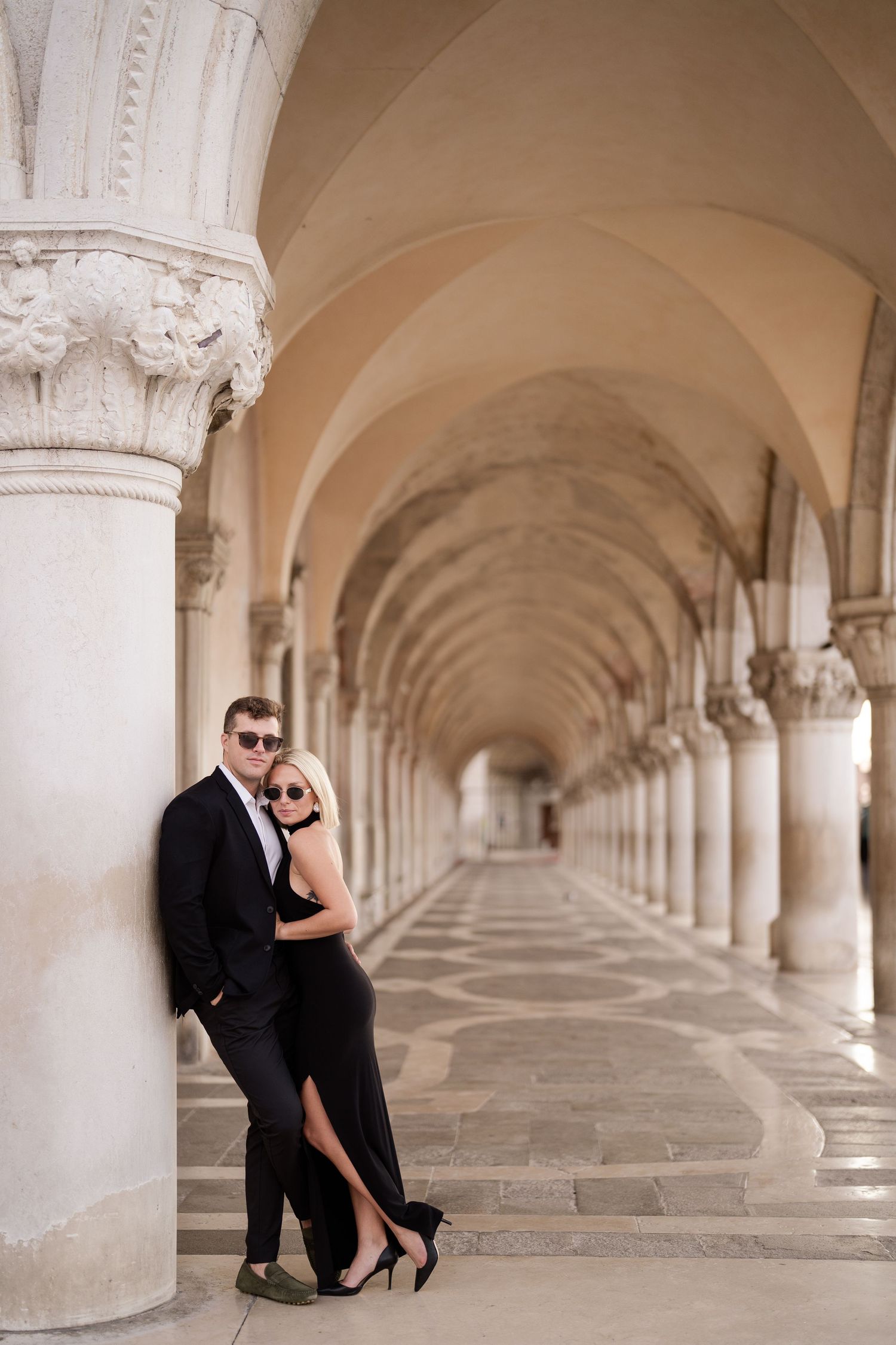 A romantic couple poses in a series of elegant photos under arched stone columns of a historic building.