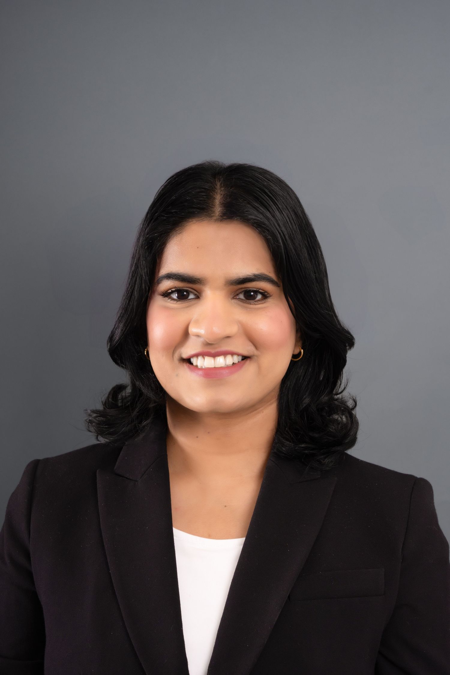 A young woman with black hair smiles confidently on a grey backdrop.