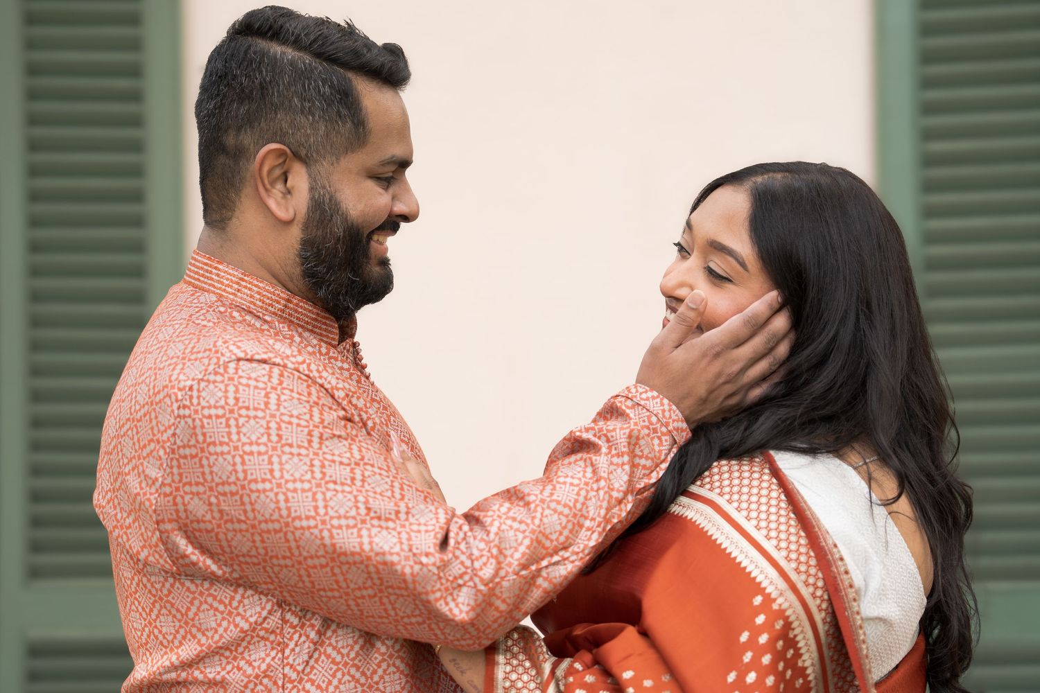 Indian couple in traditional ethnic wear sharing a tender moment, man gently touching woman's face outdoors.