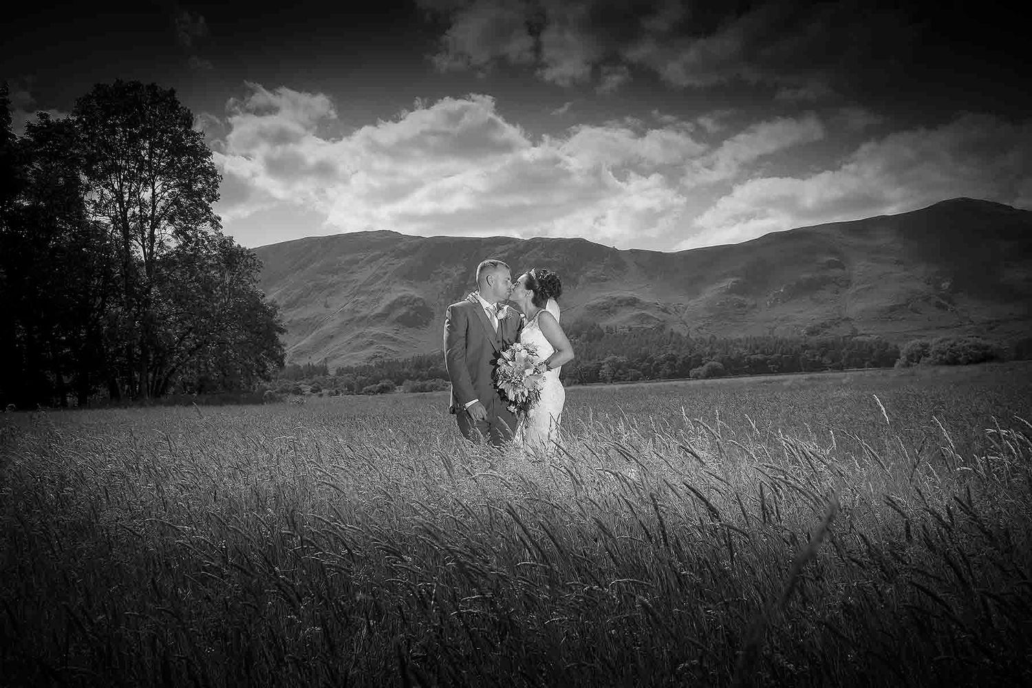 A couple embracing in a field with mountains in the background under a dramatic cloudy sky.