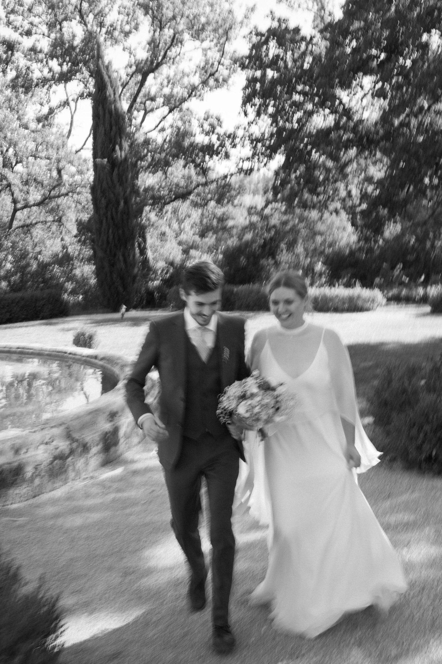 Dynamic sequence of a couple running through a park pathway in wedding attire.