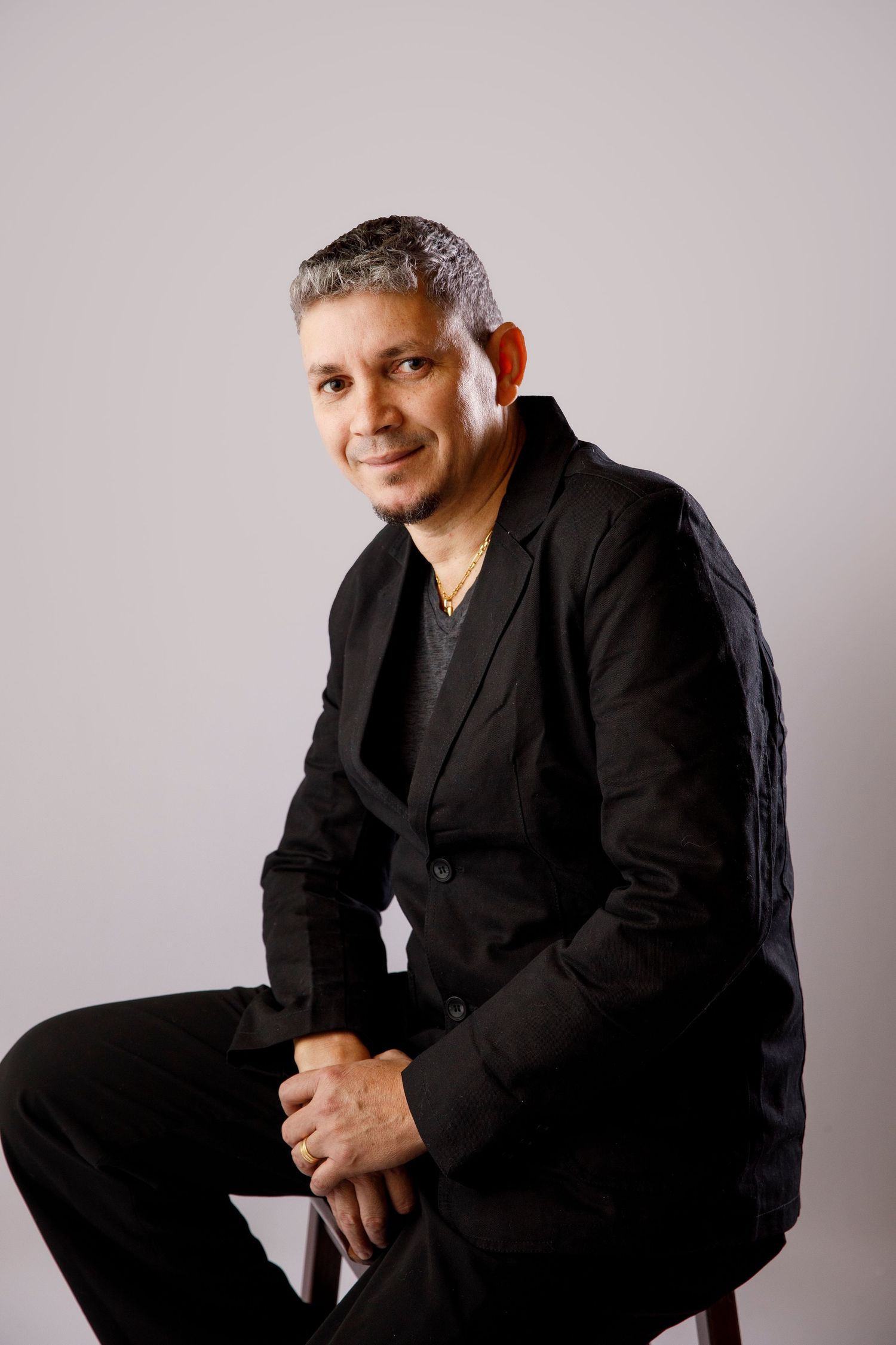 Studio portrait of person in black blazer against light gray background.