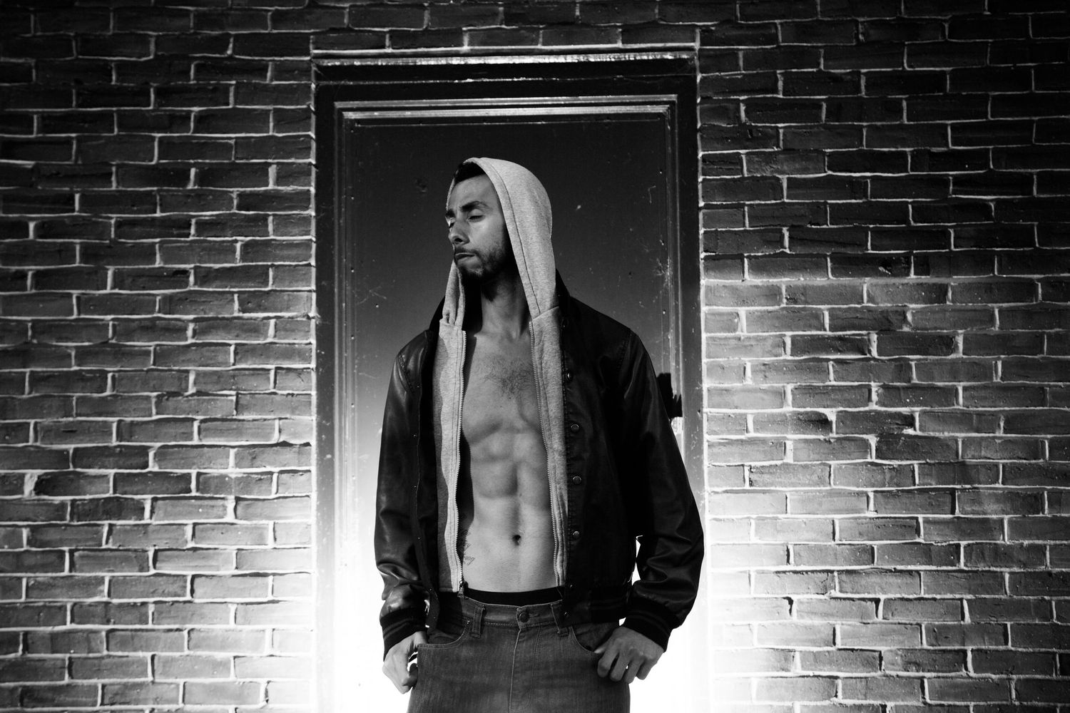 Dramatic black and white portrait of person in hoodie against brick wall.