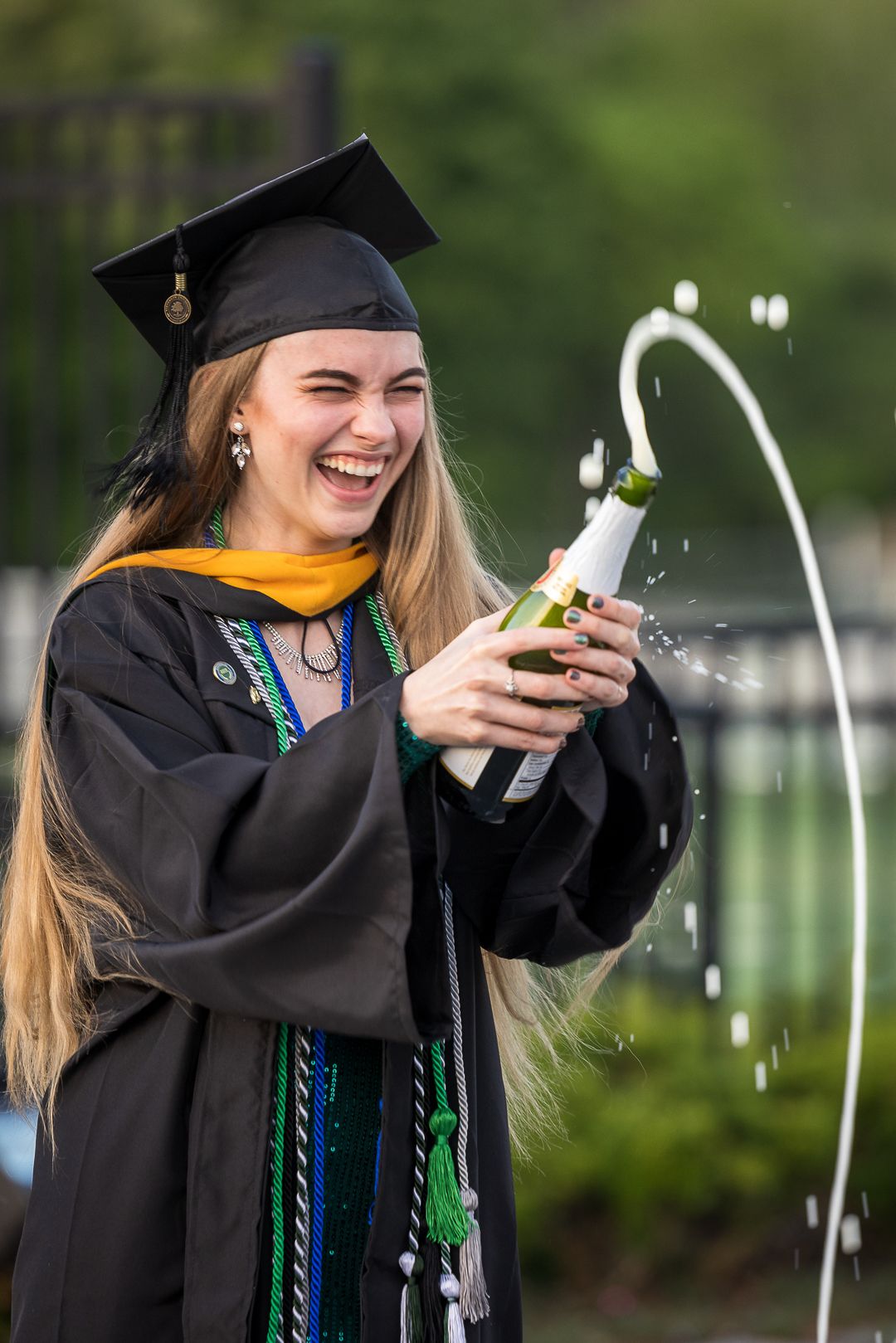 Graduate in black cap and gown smiles while taking photos during commencement ceremony.