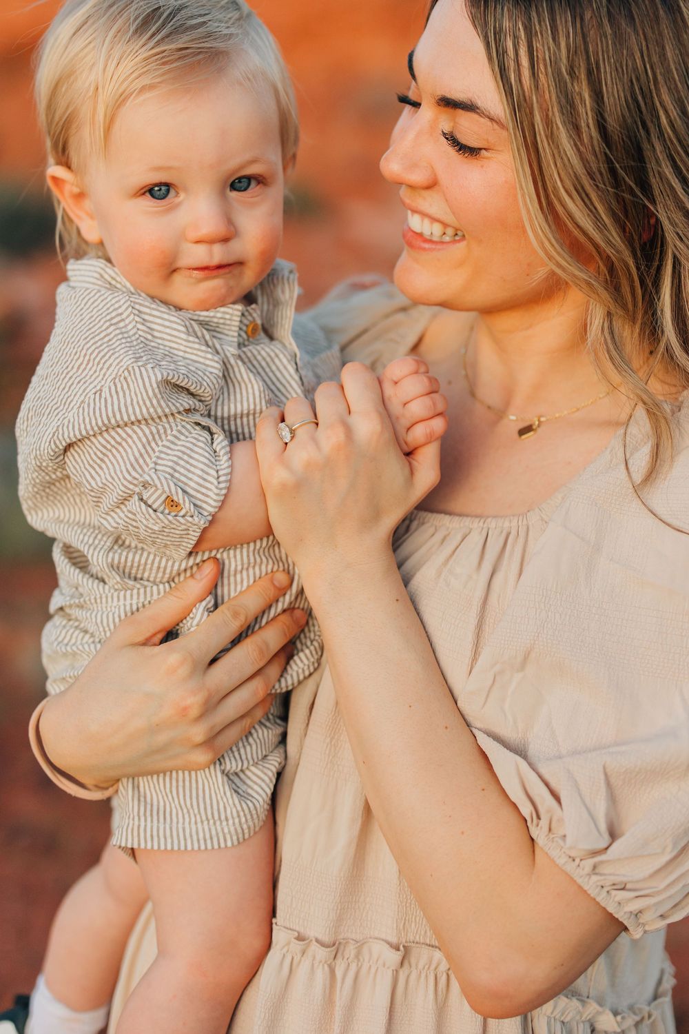A smiling woman holds a happy baby in a cozy, warm-toned outdoor setting.