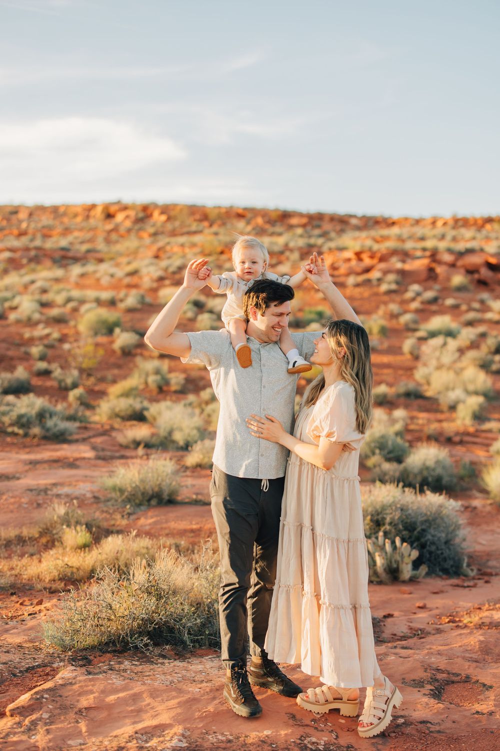 A happy family poses for a portrait in a desert landscape, with a young child in the center.