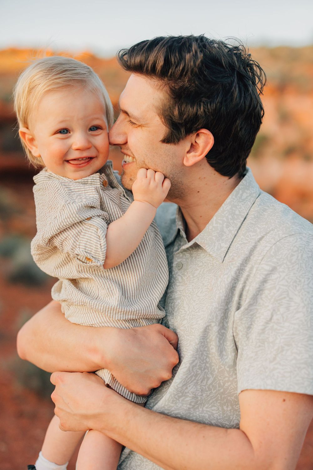 A man lovingly holds and interacts with a cheerful baby in a scenic outdoor environment.