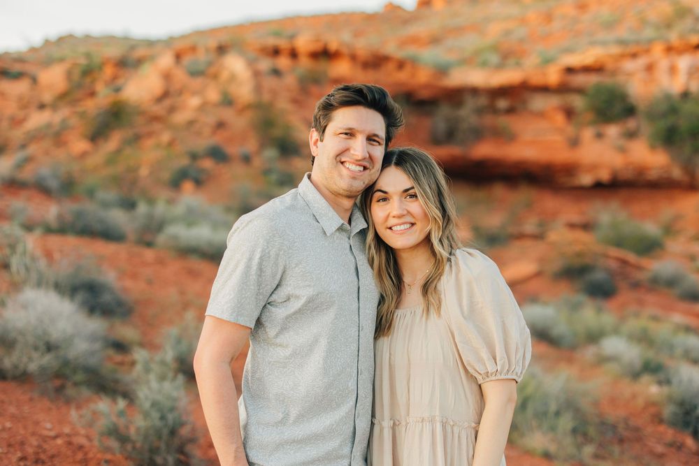 A smiling couple standing together in a beautiful desert setting with a backdrop of colorful rock formations.