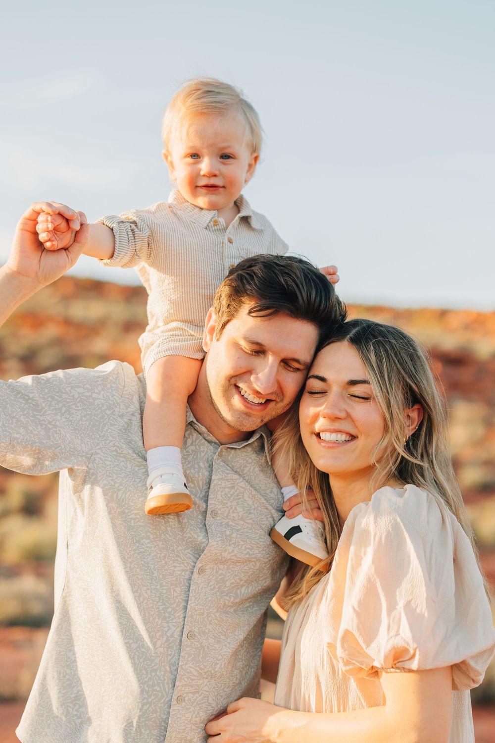 A happy family with a smiling baby being held by the parents in a natural outdoor setting.