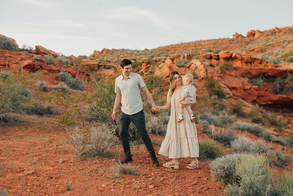 A couple standing in a scenic desert landscape with red rocks and shrubs.
