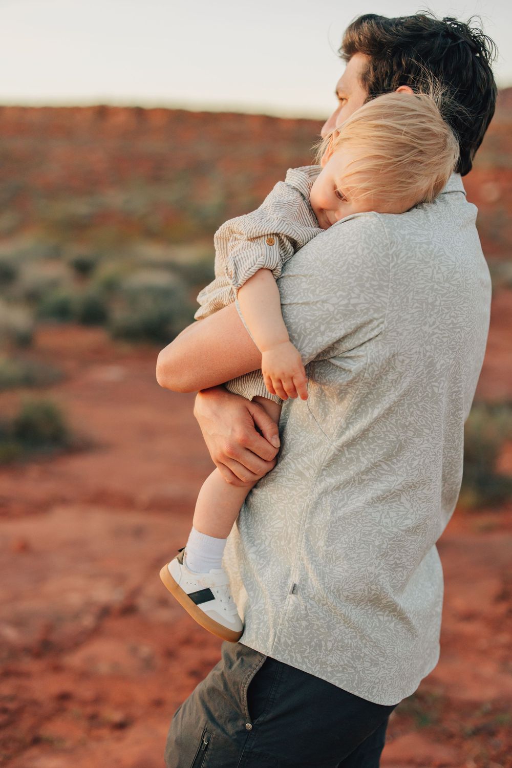 A father tenderly holding and comforting his young child in a serene outdoor setting.
