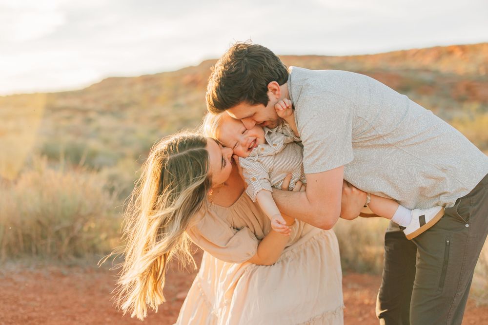 A couple embraces lovingly in a field during a sunset, with the woman's long hair flowing in the wind.