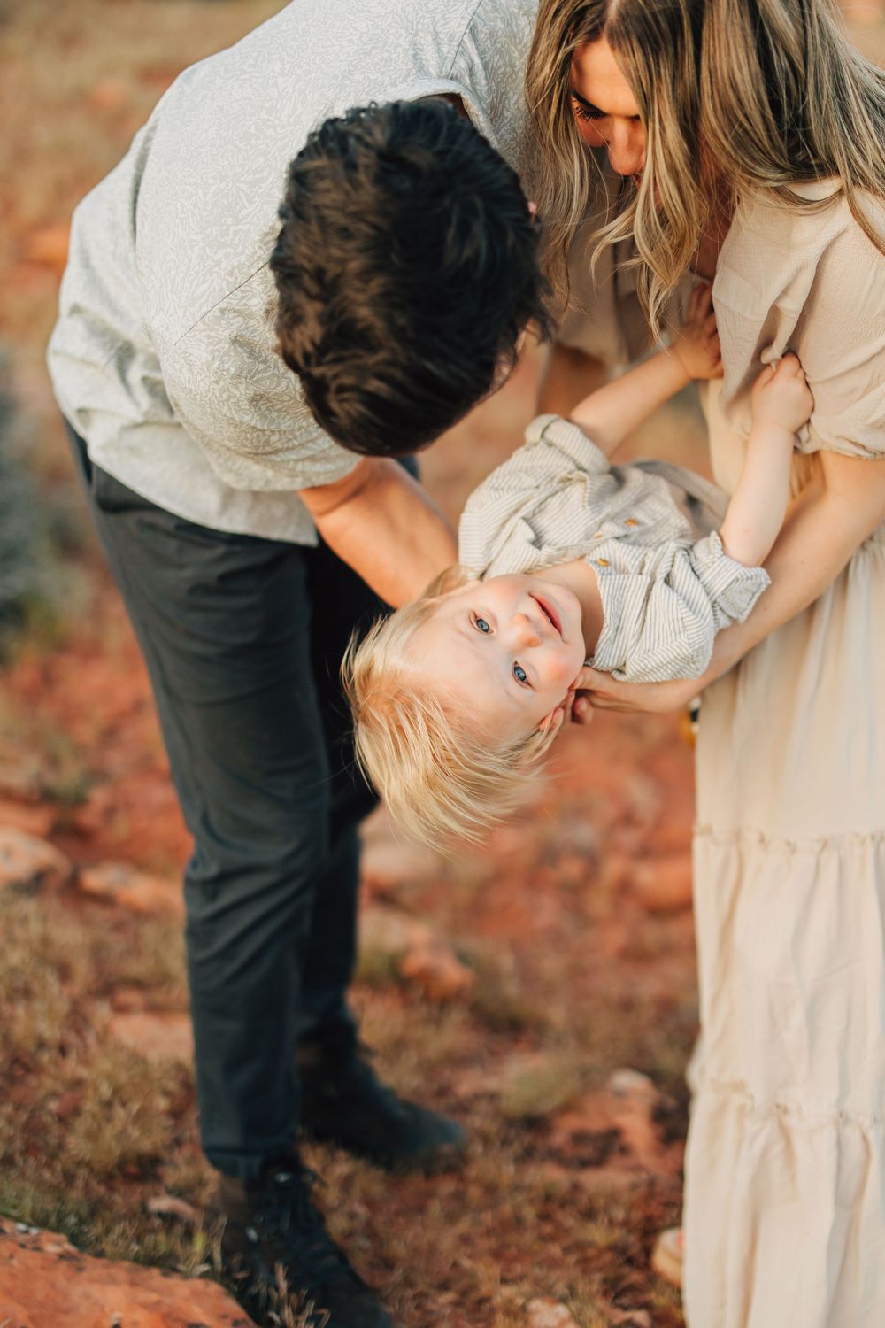 A man and a woman are embracing and leaning back in a field with a rustic, natural background.