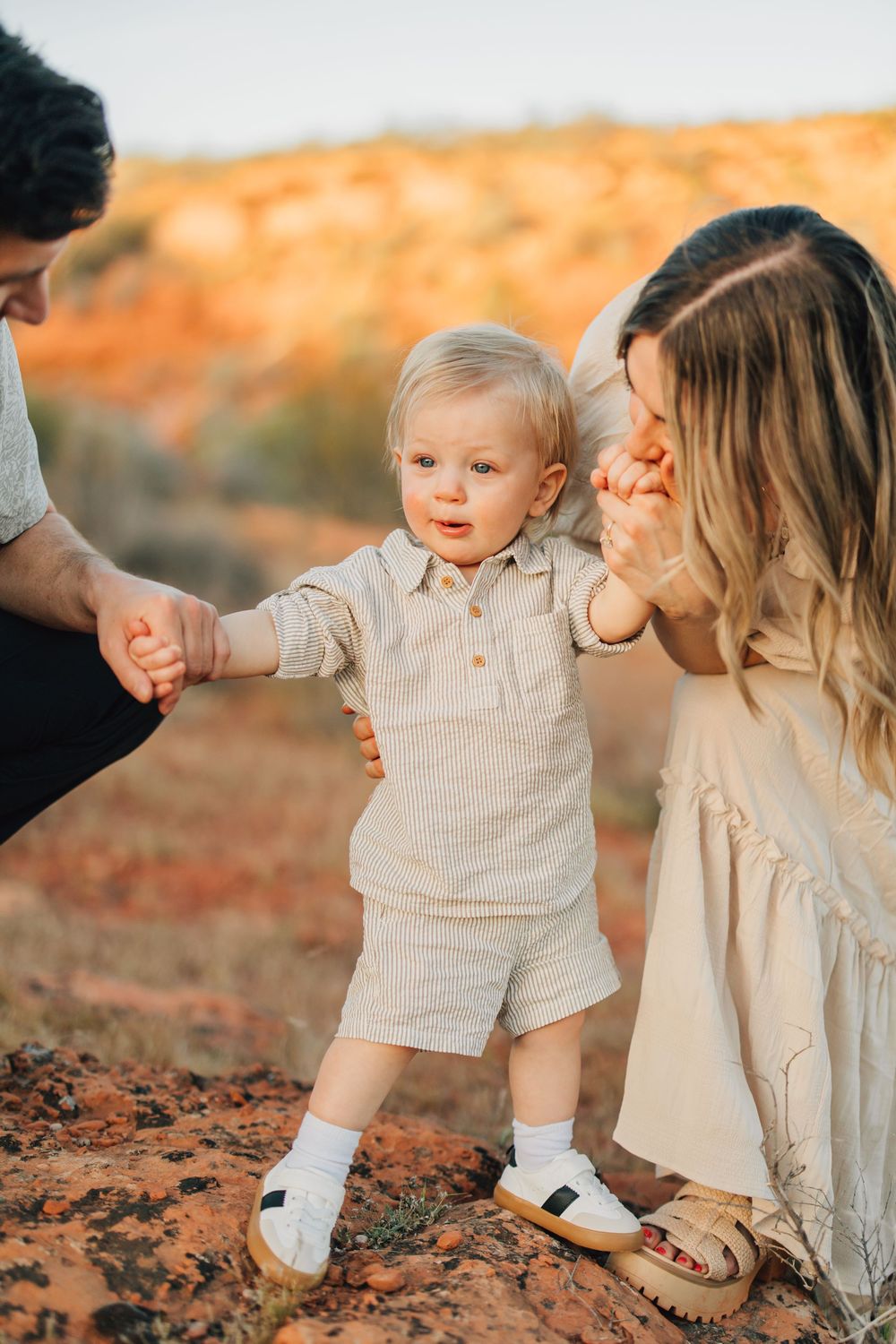A young family enjoys a moment together in a beautiful outdoor setting, with a toddler being held by the parents.