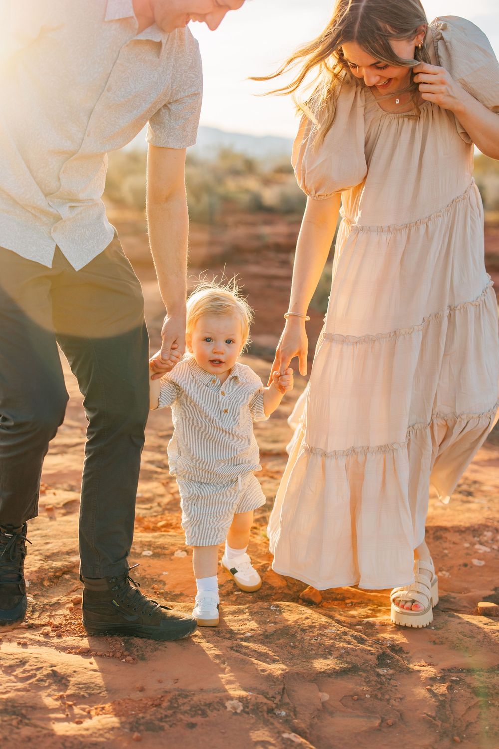 A young family walks together in a scenic outdoor setting, with a toddler in the middle.