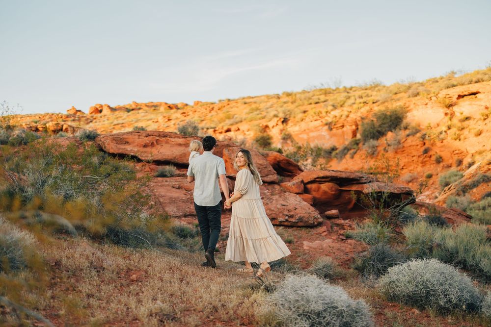 A couple stands together on a rocky, arid landscape with a scenic desert backdrop.