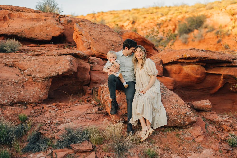 A couple standing in a desert landscape with red rock formations in the background.