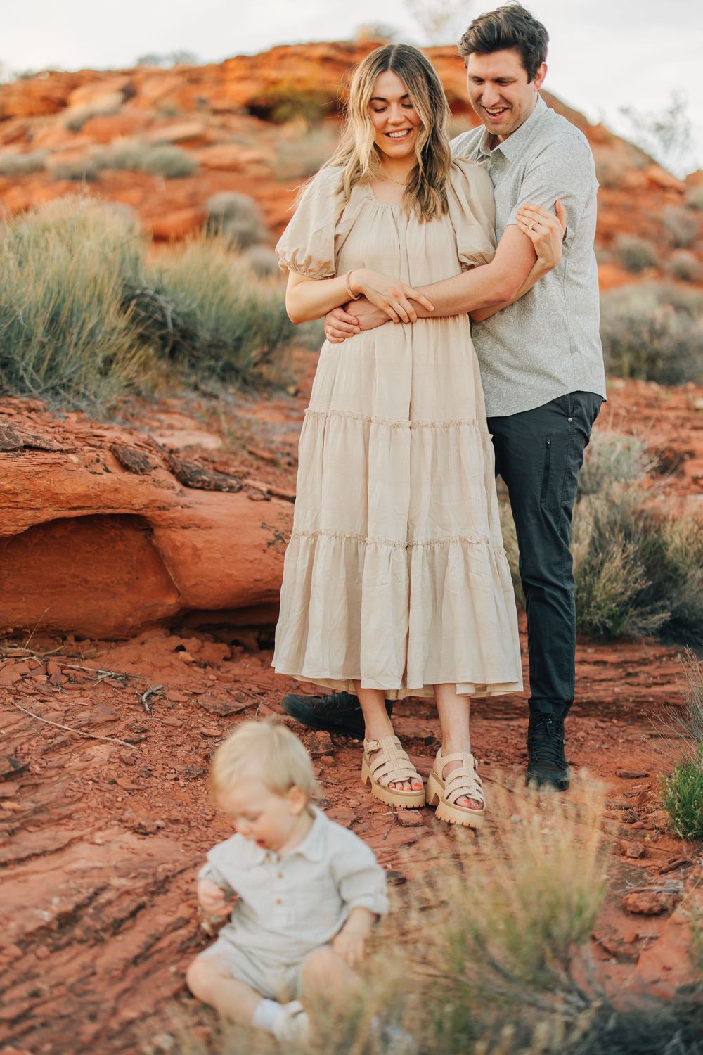 A couple stands together in a desert landscape, with a young child in the foreground.