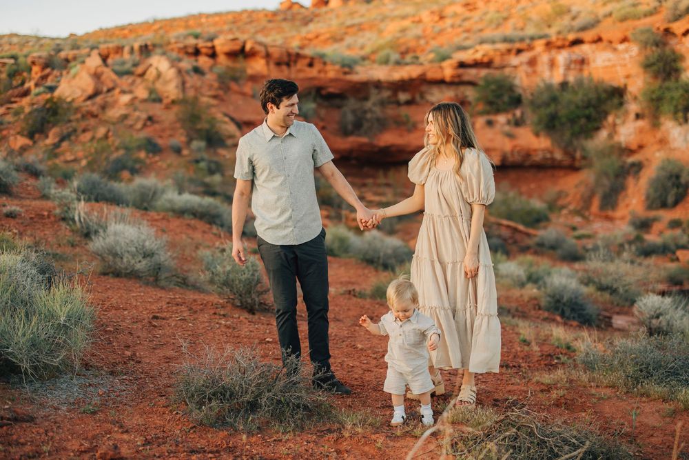 A couple walks hand-in-hand with their young child on a scenic desert trail surrounded by red rock formations.